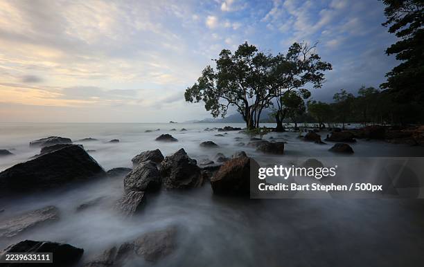 serene sunset over a rocky seascape with lush coastal trees and ethereal water movement,thailand,koh chang - koh chang stock pictures, royalty-free photos & images