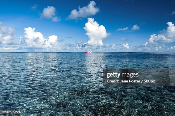 scenic view of a vast blue sea under a bright sky with white clouds and a distant boat,maldives - indian ocean stock pictures, royalty-free photos & images