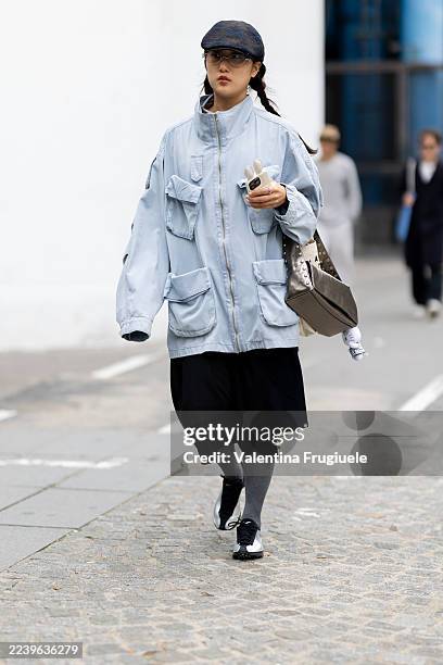 Guest wears an oversized light blue field jacket with multiple cargo pockets, layered over a black knee-length skirt, paired with gray knee-high...