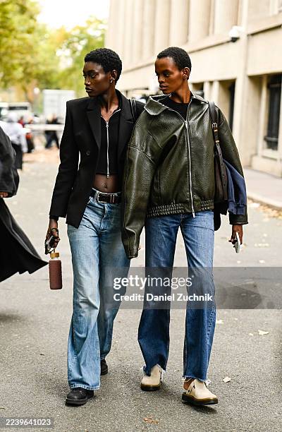 Model is seen wearing a black blazer, black zippered sweater, blue jeans and black belt with a model wearing a green jacket, blue jeans and brown bag...