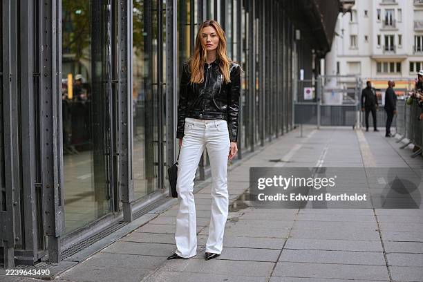 Phoebe Tonkin wears long wavy light brown hair with blonde highlights, middle part, a black leather satchel bag with silver hardware, a black patent...