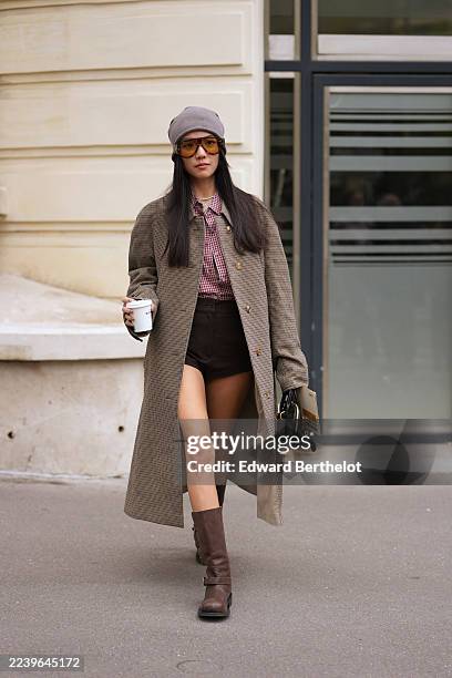 Yoyo Cao wears long straight black hair with a center part, amber-tinted sunglasses with brown frames, a short white pearl necklace, a black leather...