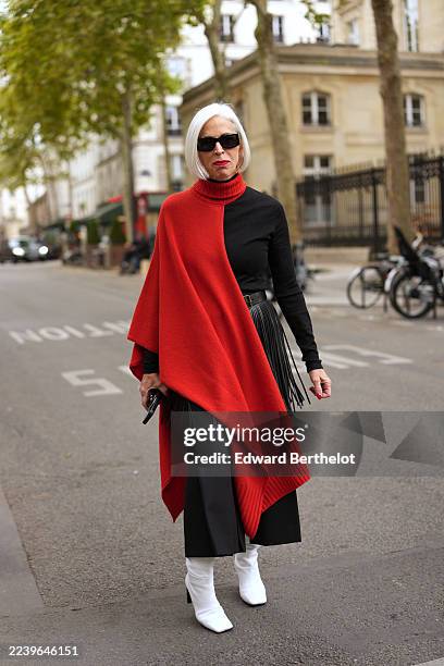 Guest wears white chin-length bob hairstyle with a side part, black rectangular sunglasses, gold hoop earrings and gold rings, red ribbed turtleneck...