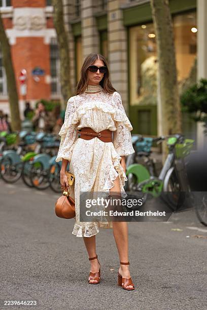 Danielle Copperman wears long straight brown hair with a center part, oversized black sunglasses, a gold ring, a brown leather top-handle bag with...