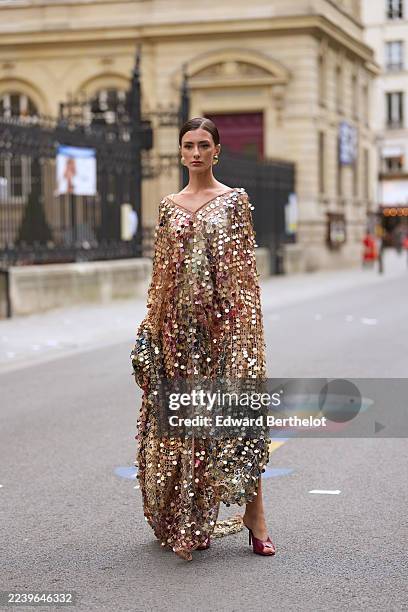 Guest wears hair pulled back into a low bun with a center part, dark brown, large gold-tone hoop earrings, a floor-length off-the-shoulder cape dress...