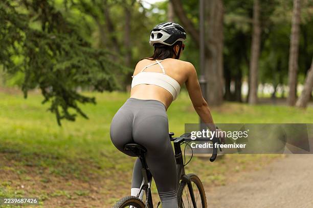 athletic woman cycling on park trail in helmet, white top, and gray leggings - nature park stock pictures, royalty-free photos & images