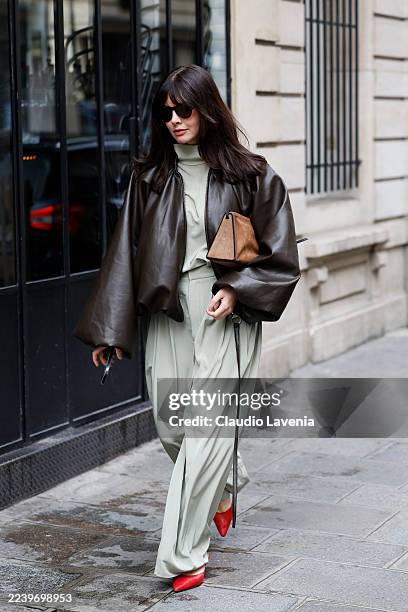 Guest wears light green blouse, matching trousers, brown leather bomber jacket, beige suede bag, red heels, outside Sacai, during the Womenswear...