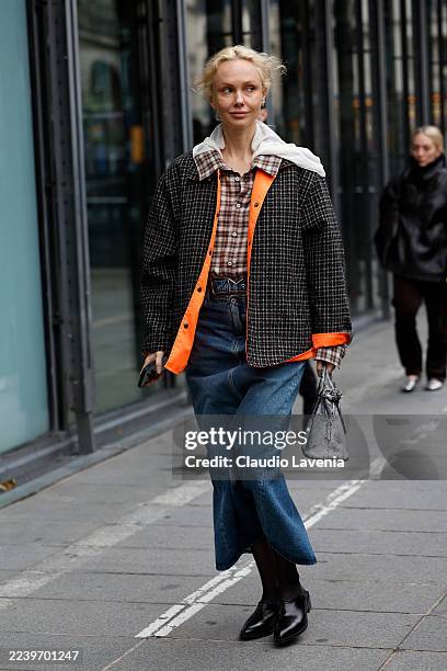 Olga Karput wears brown checked shirt, black and beige checked jacket with orange inside lining, blue denim skirt, black tights, black loafers, grey...