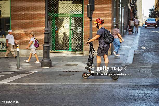 young man riding electric scooter through central madrid - trotinete imagens e fotografias de stock