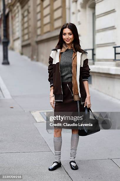 Nathalie Fanj wears grey top, beige suede jacket with brown and cream jacket on top, brown midi skirt, black Miu Miu bag, grey socks, black Miu Miu...
