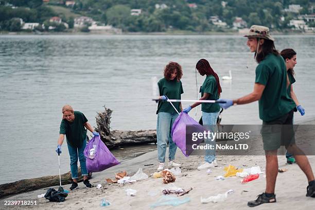 volunteers cleaning polluted river bank collecting trash - public service stock pictures, royalty-free photos & images