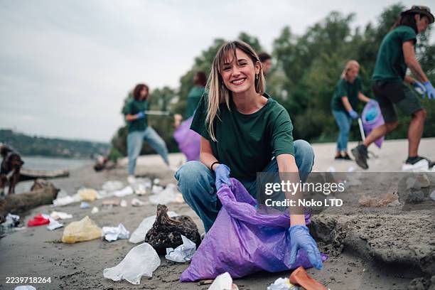 young woman volunteering cleaning polluted beach - public service stock pictures, royalty-free photos & images