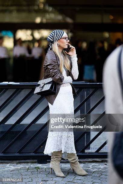 Guest wears brown glasses, a white lace long sleeved long dress, beige suede pumps, a brown leather jacket, silver earrings and a black leather...