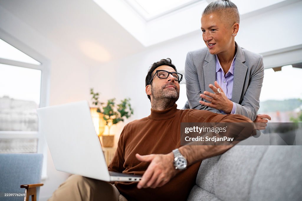 A male colleague glances at a female coworker while working on a laptop in a light-filled office