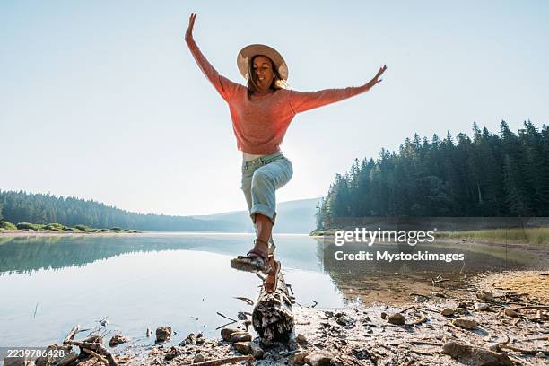 mujer haciendo equilibrio sobre troncos junto a la orilla del lago - una mujer de mediana edad solamente fotografías e imágenes de stock