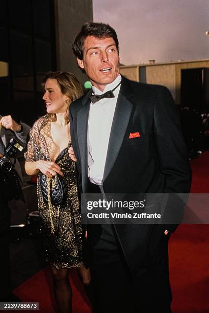 American actress and singer Dana Morosini, wearing a sheer gold evening wrap over a black dress, and her partner, American actor Christopher Reeve,...