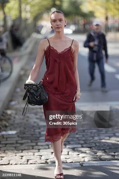 Kelys Guillouet is seen wearing gold hoop earrings, a burgundy lace-trimmed camisole slip dress, white and gold bangles, carrying a black leather...