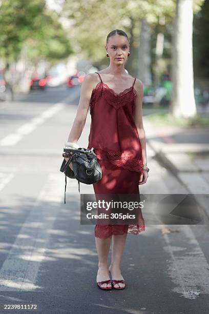 Kelys Guillouet is seen wearing gold hoop earrings, a burgundy lace-trimmed camisole slip dress, white and gold bangles, carrying a black leather...