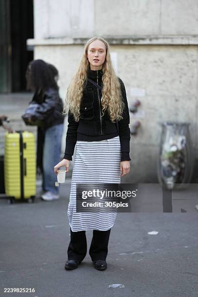 Hella Thomale is seen wearing a black zip-up jacket, a DKNY grey and white striped midi dress layered over black pants, black shoes, and carrying a...