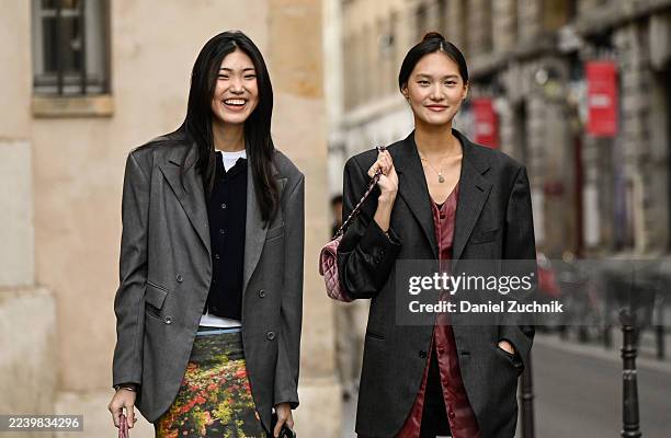 Model is seen wearing a gray blazer, black cardigan, white shirt, floral print skirt, gray leggings, black shoes and red bag with a model wearing a...
