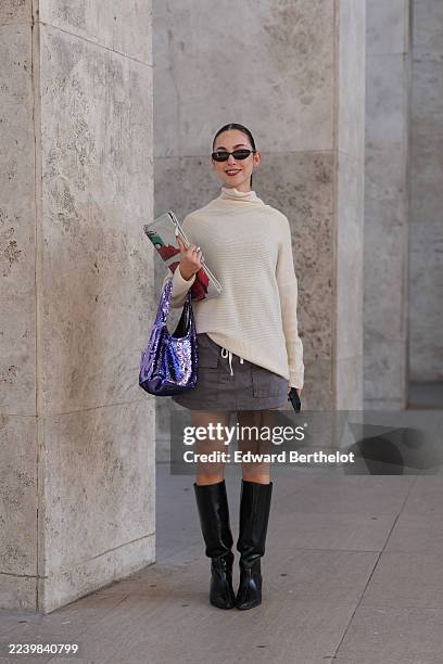 Guest wears hair slicked back into a low bun with a center part, black rectangular sunglasses, multiple silver rings, a clear PVC sequins clutch bag...