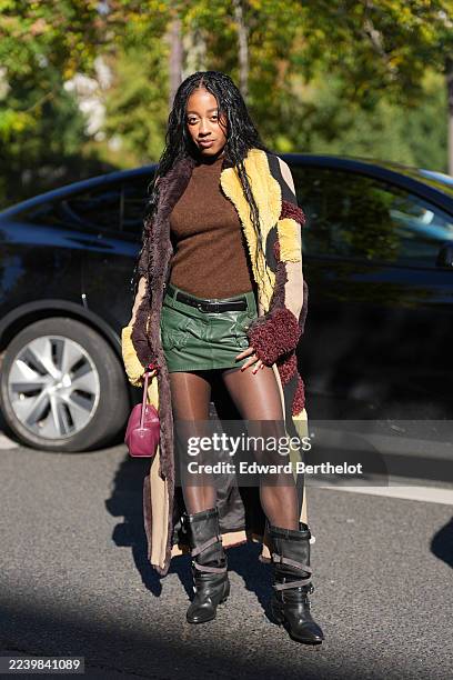 Guest wears long black braided hair with a center part, a small magenta leather top-handle bag, a long patchwork shearling coat in tan, burgundy,...