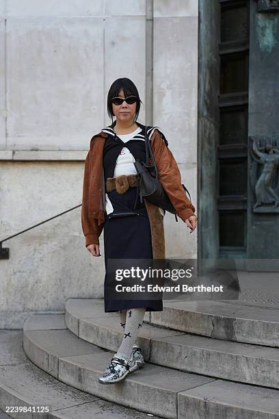 Guest wears black straight hair of medium length with blunt bangs, narrow black cat-eye sunglasses, a black leather shoulder bag, a white crewneck...
