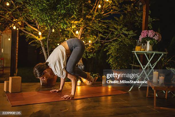 woman practicing arm balance yoga pose outdoors at night amid candlelight - homeostasis stock pictures, royalty-free photos & images