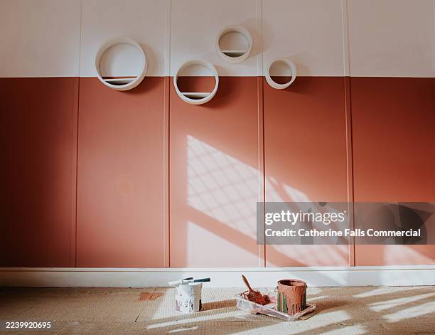 wide shot of a freshly painted room - the colour choice is a terracotta colour. paintbrushes, and messy tins sit on the floor in front of the wall - freshly painted stock pictures, royalty-free photos & images