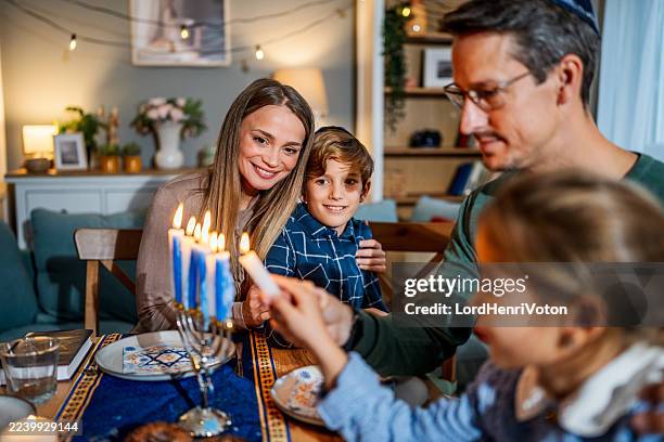 la famille célébrant hanoukka, allumant des bougies sur la menorah - juif photos et images de collection