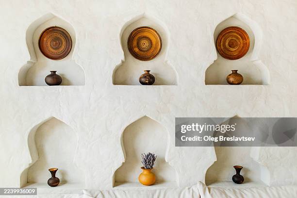 three arched niches display round plates and small pots on white walled wall. eastern interior decor. - niche stock pictures, royalty-free photos & images