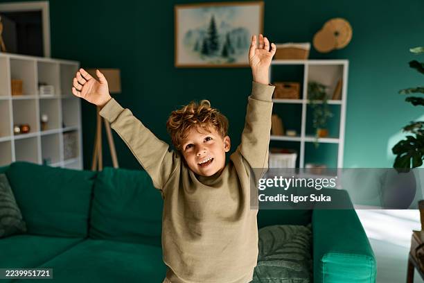 young boy cheering triumphantly with arms raised indoors - one boy only stock pictures, royalty-free photos & images