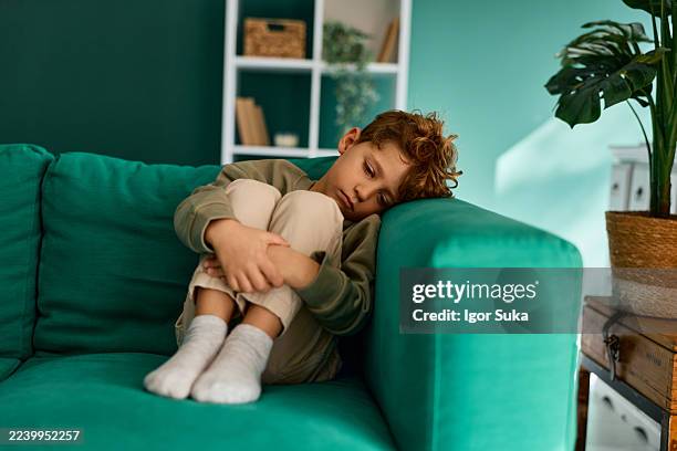 sad young boy sitting alone on couch feeling depressed - child depression stock pictures, royalty-free photos & images