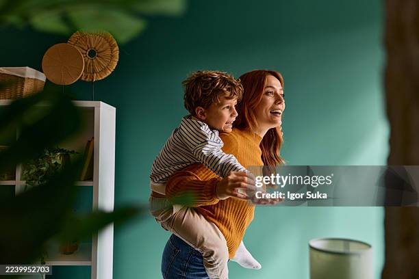 mother giving son piggyback ride at home - mother son stock pictures, royalty-free photos & images
