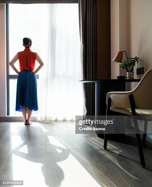 rear view of young woman opening curtains and looking out of the window - hand on hip stock pictures, royalty-free photos & images