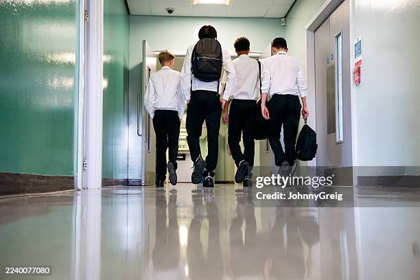 surface level view of teenage boys walking on floor in school corridor, rear view - schooljongen stockfoto's en -beelden
