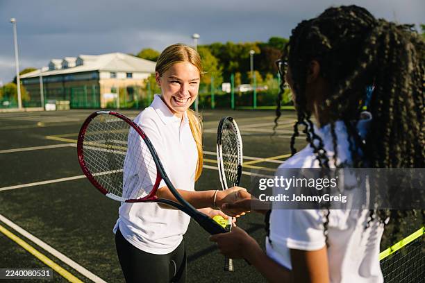 two teenage girls holding tennis racquets and shaking hands after game of tennis, smiling - newcastle upon tyne stock pictures, royalty-free photos & images