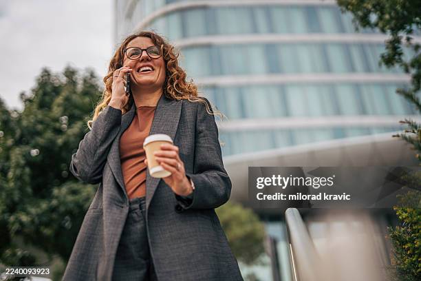 businesswoman talking on phone outdoors enjoying coffee break - adulation stock pictures, royalty-free photos & images