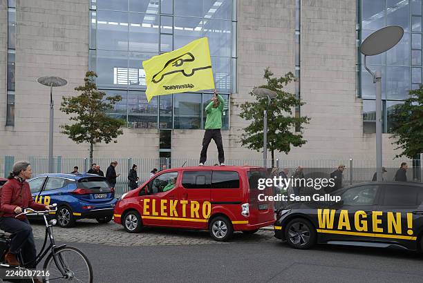 Greenpeace activist waves a flag while standing on an electric car in front of the Chancellery while inside Chancellor Friedrich Merz and other...