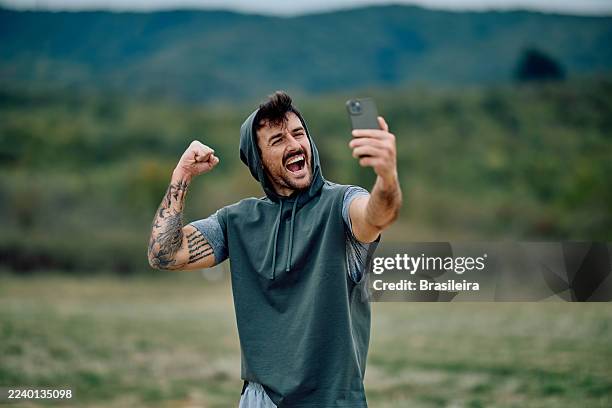 atleta masculino celebrando el éxito del entrenamiento tomándose una selfie al aire libre - flexionar los músculos fotografías e imágenes de stock