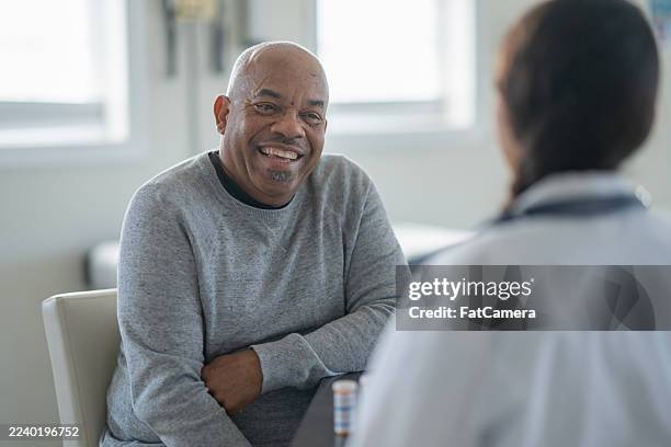 feliz hombre afroamericano mayor sonríe durante la conversación con el médico en la clínica, chequeo médico amistoso - atención primaria fotografías e imágenes de stock