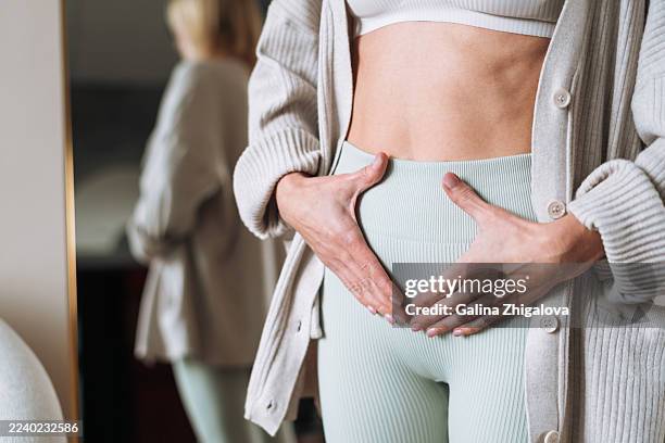 woman holding lower abdomen at home, portraying self-care during menstrual pain or bloating discomfort - inflamação imagens e fotografias de stock