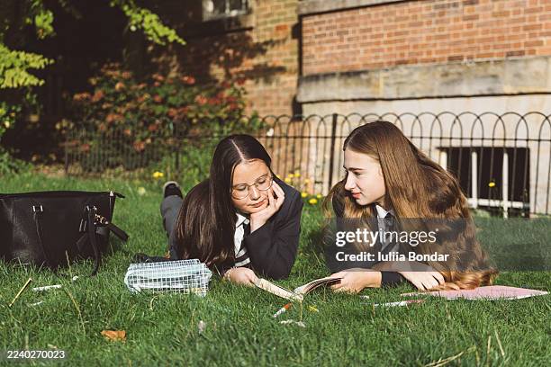 two schoolgirls reading and studying together on grass - educational subject stock pictures, royalty-free photos & images