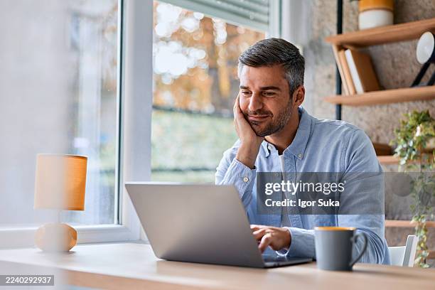hombre trabajando en la computadora portátil en la oficina doméstica - hombres de mediana edad fotografías e imágenes de stock