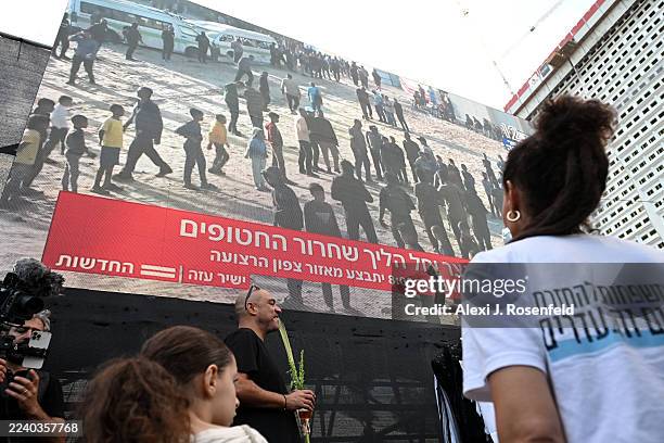 People watch a large screen broadcasting a live feed of Gaza, as they wait for the start of the hostage release at Hostages Square on October 13,...