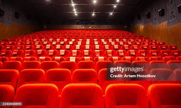 empty cinema auditorium with rows of plush red seats creating an immersive viewing experience, showing the quiet anticipation of a movie screening or a cultural event - projectie stockfoto's en -beelden