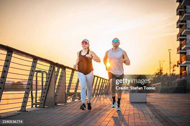carrera enérgica al amanecer a lo largo del paseo marítimo - el trabajo en equipo hace que el sueño funcione fotografías e imágenes de stock