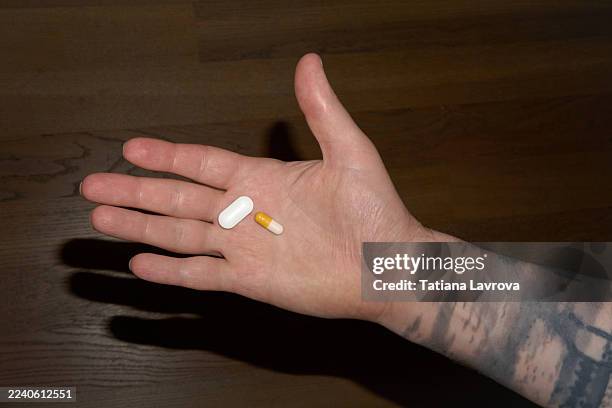 hand with pills on palm, close-up view of two tablets on a wooden background - bescherming tegen corona stockfoto's en -beelden