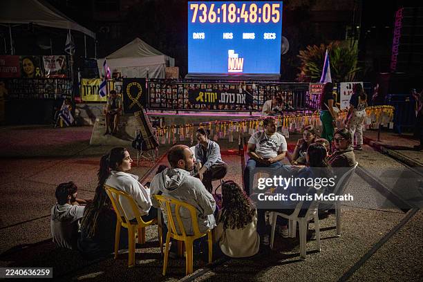 People sit and talk in front of a clock counting the days the hostages have been in captivity at Hostages Square on October 13, 2025 in Tel Aviv,...