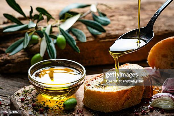 mediterranean food: extra virgin olive oil pouring from spoon to a bread slice on rustic wooden table. green olives, pepper, salt and garlic. savory food - italiaanse keuken stockfoto's en -beelden